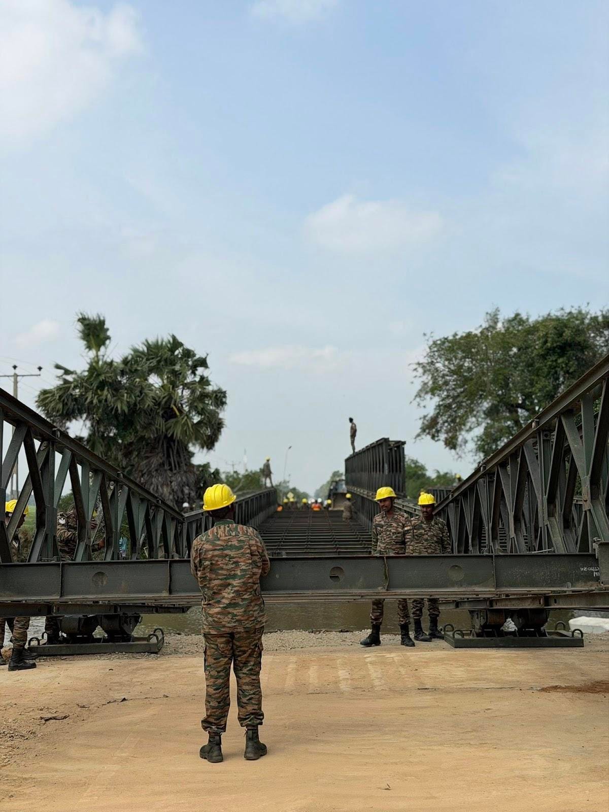 Indian Army officers work to assemble a temporary Bailey bridge on the A035 road after cyclone-related damage disrupted connectivity.